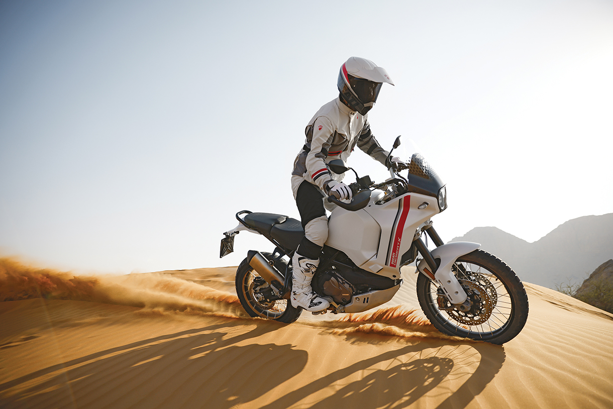 Bike rider wearing helmet and full racing gear on an off-road Ducati white motorcycle in the desert